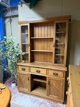 Load image into Gallery viewer, A classic oak dresser combining practical storage with timeless appeal. This piece features a spacious upper section with two cupboards and shelving, while the lower section offers three short drawers and two single cupboards—ideal for displaying treasures or storing everyday items. Structurally sound with minor cosmetic marks consistent with age and use. Designed to separate into two sections for convenient moving and placement. Perfect for adding warmth and character to any room.
Delivery Available
Over