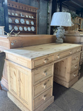 Load image into Gallery viewer, A solid pine double pedestal desk in good structural condition, stripped to reveal its natural grain and warm timber character. Features eight small dovetail-jointed drawers plus one long drawer for practical storage. The piece disassembles into three sections for convenient transport and repositioning.
Well-suited for a home office or study, this desk offers authentic craftsmanship and timeless appeal. The natural finish allows the wood character to shine; consider applying wax or oil for added protection