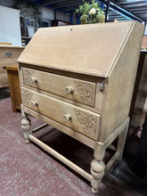 Load image into Gallery viewer, A beautiful stripped oak bureau revealing the wood's natural grain and character. Features a pull-down writing desk for functionality, paired with two spacious dovetail-jointed drawers adorned with delicate floral carvings. The bare wood finish offers authentic period appeal and accepts wax or oil beautifully for added protection and lustre. Ideal for those seeking genuine vintage craftsmanship with practical storage.
Delivery Available
Overall Dimensions
75cm wide x 40cm deep x 96cm high 