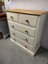 Load image into Gallery viewer, A charming solid pine chest of drawers that brings rustic character to any room. Featuring five generously proportioned drawers—two dovetail-jointed compartments above three spacious ones—this piece offers excellent storage versatility. The light beige painted base provides a soft, neutral foundation, while the natural waxed pine top showcases the wood's warm grain. Built to last with sturdy construction and in wonderful condition, it's a timeless addition to country-style interiors.
Delivery Available
Ov