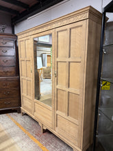 Load image into Gallery viewer, A magnificent Waring & Gillow oak wardrobe, restored to showcase its natural grain and character. This substantial piece features generous storage across one double and one single cupboard, each fitted with a hanging rail for organised dressing. The vintage mirror retains authentic patina that enhances its period appeal. Stripped back to bare wood, it would benefit from a protective wax finish to suit your décor. Thoughtfully designed to disassemble into four sections, making transport and placement str