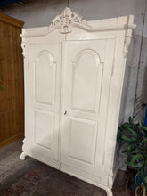Load image into Gallery viewer, Discover the timeless elegance of this antique pine wardrobe, a statement piece with authentic character and French-inspired style. Finished in gloss white, it shows gentle patina that adds to its vintage charm—ideal for a refresh if desired. Structurally sound and in good condition, this wardrobe splits down the middle for convenient transport and repositioning. Inside, a sturdy hanging rail provides practical storage for your wardrobe essentials. Perfect for period homes, eclectic interiors, or anyone see