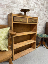 Load image into Gallery viewer, A charming vintage pine bookcase with authentic character. Structurally sound and ready for use, this piece features two practical drawers and two shelves for storage. As a pre-loved item, it bears the natural marks and patina of age—including some missing trim on one drawer—which adds to its vintage appeal. A thorough clean will restore its warmth and beauty. Ideal for those who appreciate genuine period furniture with history and charm.
Delivery Available
Overall Dimensions
75cm wide x 22.5cm deep x 10