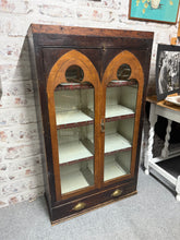 Load image into Gallery viewer, A magnificent gothic-inspired oak display cupboard that combines character with practicality. This well-maintained piece showcases authentic vintage charm, with its distinctive architectural style making a bold statement in any room. The glass-fronted doors reveal three generous shelves perfect for showcasing treasured collections, while a spacious base drawer provides convenient hidden storage. Despite its pre-loved history, the cupboard remains structurally robust and in overall good condition.
Delivery