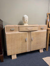 Load image into Gallery viewer, This Art Deco sideboard showcases timeless design with functional elegance. Recently stripped to reveal its natural wood finish, it displays the character of vintage furniture with light patina and minor surface marks that add to its charm. The piece offers generous storage through three dovetail-jointed drawers—two shallow and one full-width—plus a spacious double cupboard. Perfect for dining rooms, living spaces, or entryways seeking classic appeal with practical storage.
Delivery Available
Overal