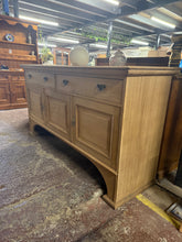 Load image into Gallery viewer, A beautifully stripped oak sideboard revealing natural grain and character. Structurally sound with authentic patina marks that add vintage appeal. Features two dovetail-jointed drawers above a double and single lockable cupboard— comes with original key. The bare wood finish invites personalisation with wax or oil to suit your décor. A versatile storage piece with genuine craftsmanship and timeless style.
Delivery Available
Overall Dimensions
183cm wide x 57cm deep x 96cm high