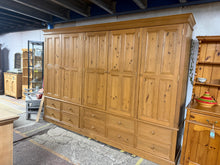 Load image into Gallery viewer, This spacious solid pine wardrobe combines practical storage with timeless craftsmanship. Featuring two double hanging cupboards, a shelved cupboard, and ten dovetail-jointed drawers, it offers versatile organisation for any bedroom. The piece is structurally sound and in good overall condition, with minor surface marks consistent with age and use. Designed for convenience, it disassembles into six sections, making transport and installation straightforward. An excellent choice for those seeking substantial