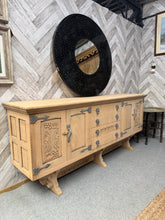Load image into Gallery viewer, A beautiful stripped oak sideboard showcasing natural wood grain throughout. Recently stripped back to bare wood, it would benefit from a protective coat of wax to enhance and preserve the finish. Generously proportioned with practical storage: two double cupboards and four long dovetail-jointed drawers provide ample space for dining essentials. Two cupboards and one drawer feature detailed carving, adding character and craftsmanship that makes this an impressive focal point for any living or dining room. A