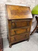 Load image into Gallery viewer, A charming narrow oak bureau in structurally sound condition. This well-loved piece features a pull-down writing desk and three spacious dovetail-jointed drawers, offering practical storage for any room. Light wear consistent with age and use; no significant damage. Ideal for those seeking authentic vintage character with genuine functionality.
Delivery Available
Overall Dimensions
61cm wide x 40cm deep x 100cm high