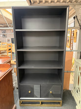 Load image into Gallery viewer, A striking geometric bookcase that combines practical storage with contemporary style. Featuring three sturdy fixed shelves and two convenient drawers, it offers ample space for books, décor, and everyday essentials. The sleek black finish complements any interior scheme. While this piece shows marks, it remains fully functional and structurally robust.
Delivery Available
Overall Dimensions
90cm wide x 45cm deep x 190cm high   