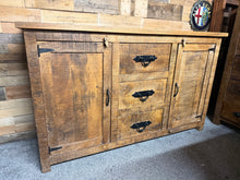Load image into Gallery viewer, Crafted from solid wood, this rustic sideboard combines timeless character with practical storage. Two cupboards with internal shelving and three central drawers provide generous space for dining essentials, linens, or display pieces. Minor surface marks add to its authentic rustic appeal, while sturdy construction ensures lasting durability. An ideal statement piece for farmhouse, cottage, or eclectic interiors seeking warmth and functionality.
Delivery Available
Overall Dimensions
150cm wide x 45cm dee