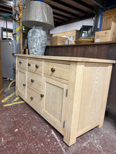 Load image into Gallery viewer, This stripped oak sideboard showcases beautiful natural wood grain and authentic craftsmanship. Returned to its raw state, it invites personalisation with your choice of finish—a protective wax coat will enhance both appearance and durability. Generously proportioned storage includes two short dovetail-jointed drawers, two deep drawers, two long drawers, and two single cupboards, offering flexible organisation for any room. A versatile piece that brings warmth and character to traditional or contemporary in