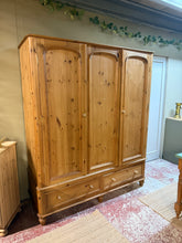 Load image into Gallery viewer, A characterful vintage pine triple wardrobe with genuine period appeal. Structurally sound with quality dovetail jointed drawers and a hanging rail for storage. One door shows warping. Dismantles into three sections for convenient transport and placement. Surface patina and marks add to its vintage charm and can be refreshed with wax or paint to suit your décor. An authentic statement piece for period homes or eclectic interiors.
Delivery Available
Overall Dimensions
156cm wide x 56cm deep x 188cm high