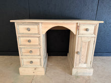 Load image into Gallery viewer, A solid pine desk with authentic character and timeless appeal. This piece has been stripped back to reveal natural wood grain and has a rough pine finish. Structurally sound and in good condition, it offers practical storage across five short drawers and a lower cupboard. The bare wood finish allows you to personalise the look with wax, oil, or paint to suit your space. An excellent choice for those seeking genuine vintage furniture with real functionality.
Delivery Available
Overall Dimensions
106cm wi