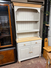 Load image into Gallery viewer, Discover the charm of this beautifully restored solid pine dresser! Stripped back to reveal its natural character, this piece features 'Worn Canvas' in colour and is complemented by natural wood plinth and top. The practical layout includes two fixed shelves perfect for display, two dovetail jointed drawers for storage, and a spacious double cupboard below. Structurally robust and in wonderful condition.
Overall Dimensions
103cm wide x 45cm deep x 210cm high
DELIVERY AVAILABLE      
For our other items