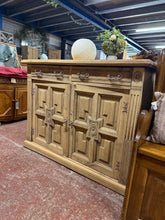 Load image into Gallery viewer, A striking carved oak sideboard with authentic character and timeless appeal. This piece has been stripped back to reveal the natural wood grain, creating a warm, organic finish that would benefit from a wax treatment to maintain its beauty and protect the surface. The sideboard features two dovetail-jointed drawers offering secure storage, positioned above a spacious double cupboard with a single shelf—ideal for displaying treasured items or concealing everyday essentials. As a pre-loved piece, it bears th
