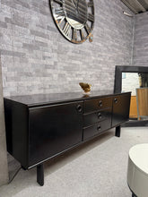 Load image into Gallery viewer, A striking retro black sideboard combining timeless style with practical storage. This piece features solid construction and authentic vintage character, complete with 2 cupboards and 3 drawers—ideal for living rooms or dining spaces. Well-maintained and ready to enhance your home with mid-century appeal. It does have marks including some minor damage to one edge but nothing major.
Delivery Available
Overall Dimensions
180cm wide x 45cm deep x 74.5cm high