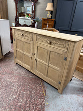 Load image into Gallery viewer, Discover the natural beauty of this stripped oak sideboard, revealing the wood's authentic grain and character. Structurally sound and ready for finishing, it's an ideal canvas for personalisation with wax or your chosen protective coating. Featuring carved drawers that add distinctive charm, this piece combines practical storage with timeless appeal. Two shallow drawers sit above a spacious double cupboard, offering ample room for your belongings. A versatile addition to any home, perfect for those who app