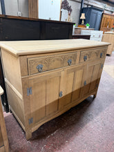 Load image into Gallery viewer, Discover the natural beauty of this stripped oak sideboard, revealing the wood's authentic character and grain. Featuring intricately carved drawer fronts that serve as a striking focal point, this piece combines form with function. Two dovetail-jointed drawers sit above spacious cupboards, offering versatile storage solutions. Structurally sound and well-maintained, it's ready to enhance any room. A protective coat of wax will help preserve its finish and bring out the wood's warmth.
Delivery Available
O