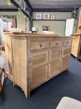 Load image into Gallery viewer, A characterful stripped oak sideboard with authentic period appeal. Natural wood finish showcases the grain and patina of age—a light wax coat will enhance protection and lustre. Generously proportioned with three dovetail-jointed drawers above a double and single cupboard, offering substantial storage for dining rooms or hallways. Honest wear and minor marks reflect its heritage.
Delivery Available
Overall Dimensions
136cm wide x 43cm deep x 86cm high