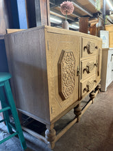Load image into Gallery viewer, A striking oak Art Deco sideboard, stripped to reveal its natural grain and patina. Features two single cupboards with internal shelving and three dovetail-jointed drawers offering generous storage. The piece is structurally sound with minor surface lifting—characteristic of vintage furniture. Ideal for those appreciating authentic period design. A light wax finish is recommended to protect the wood and enhance its warm tone.
Delivery Available
Overall Dimensions
138cm wide x 47cm deep x 92.5cm high + 9c