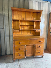 Load image into Gallery viewer, This vintage pine dresser combines rustic charm with practical storage. The upper section features three spacious shelves ideal for displaying collections or tableware, while the base offers one long drawer and four shorter drawers for concealed storage. Structurally sound and well-maintained for its age, the piece bears marks and minor surface cracks but nothing major. Splits into two sections for convenient transport and placement. Perfect for those seeking genuine vintage character with reliable everyday