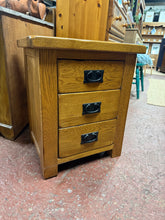 Load image into Gallery viewer, This oak furniture land bedside table combines practical storage with rustic charm. Featuring three dovetail-jointed drawers, it offers ample space for bedside essentials while the sturdy construction ensures lasting durability. The piece shows honest signs of use with minor surface marks, adding character to its rustic appeal.&nbsp;

Delivery Available

Overall Dimensions

51cm wide x 41cm deep x 59.5cm high&nbsp;

