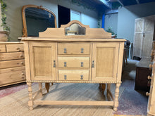 Load image into Gallery viewer, A beautiful stripped oak sideboard, restored to reveal its natural grain and character. This pre-loved piece shows gentle signs of age—minor surface marks and a small crack near one door lock that doesn't impact functionality. Features three dovetail-jointed drawers and two cupboards, one with an internal shelf, offering ample storage. The bare wood may benefit from a protective wax finish to enhance durability and appearance. Ideal for those who appreciate authentic vintage furniture with honest patina.

D
