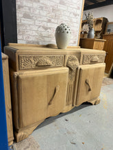 Load image into Gallery viewer, A striking Art Deco sideboard in oak, combining vintage character with practical storage. Structurally sound with authentic patina—minor marks and surface wear enhance its period appeal rather than detract from it. Features two dovetail-jointed drawers positioned above a spacious double cupboard, offering generous storage for living room essentials. An elegant statement piece that brings timeless style to any interior.

Delivery Available

Overall Dimensions

139cm wide x 50cm deep x 90cm high plus an extra
