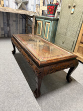 Load image into Gallery viewer, A characterful solid wood coffee table with hand-carved detailing, showcasing authentic patina from years of use. The removable glass top protects the intricate woodwork whilst maintaining its visual impact. Minor surface marks add to its vintage charm rather than detract from it. Structurally robust and ready for another chapter in a home where it'll serve as a genuine conversation starter.

Delivery Available

Overall Dimensions

101cm wide x 50cm deep x 35cm high

