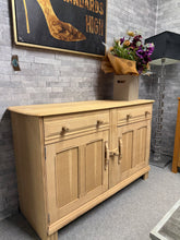 Load image into Gallery viewer, Charming stripped oak sideboard returned to its natural finish, offering versatile styling potential. Features two spacious drawers positioned above a double cupboard for generous storage. The top surface displays characteristic marks from its previous structure—perfect for personalisation with stain, paint, or wax to suit your décor. A timeless piece that rewards a little attention with beautiful results.

Delivery Available

Overall Dimensions

131cm wide x 48cm deep x 84.5cm high&nbsp;

