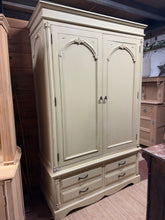 Load image into Gallery viewer, This elegant cream French-style wardrobe combines timeless design with practical storage. Structurally sound and in good overall condition, it features one hanging rail for garments and four dovetail-jointed drawers for folded items and accessories. Minor marks are present but nothing major. The piece disassembles for convenient transport and repositioning, making it ideal for those who value flexibility.

Delivery Available

Overall Dimensions

129cm wide x 60cm deep x 207cm high

