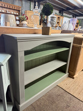 Load image into Gallery viewer, A charming two-tone green solid pine bookcase with enduring appeal. The piece is structurally sound and ready for use, bearing the subtle character marks of its history. Features two adjustable shelves, offering flexible storage solutions for books, décor, and everyday items. An excellent choice for adding warmth and functionality to any room.

Delivery Available

Overall Dimensions

121cm wide x 34cm deep x 92cm high

