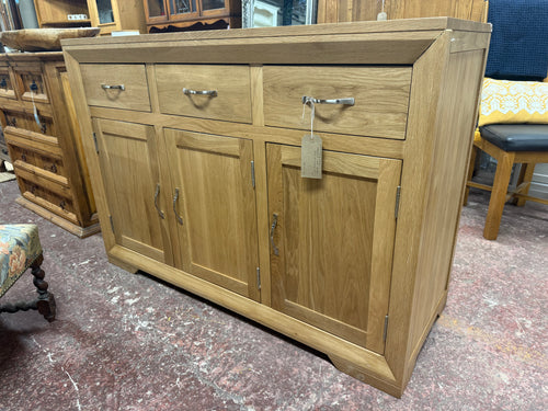 The Bevel Natural Solid Oak Large sideboard is a highly-functional unit with a refreshingly simple design. Made from beautiful solid oak timbers, it is characterised by the bevelled frame with mitred joints and gracefully angled feet. The two doors on the left side of the unit open to reveal a conjoined cupboard space, while the remaining conceals a height-adjustable shelf for taller items. The three large drawers are ideal for storing linen or cutlery and have all been made using traditional dovetail joint