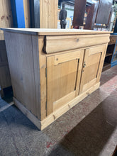 Load image into Gallery viewer, Discover the timeless appeal of this beautifully stripped antique pine sideboard. Restored to reveal its natural grain and character, this piece combines authentic craftsmanship with practical storage. Features a secret dovetail-jointed drawer and spacious double cupboard with internal shelf—perfect for displaying treasures or keeping essentials organised. Structurally sound with minor patina marks that add to its vintage charm. A light wax finish will enhance and protect the wood. An elegant addition to an
