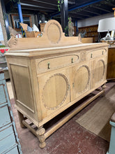 Load image into Gallery viewer, A French-style oak sideboard stripped back to reveal its natural beauty and patina. The sturdy frame houses two dovetail-jointed drawers and two cupboards, delivering practical storage with authentic period appeal. Built to last, this solid piece remains in good structural condition and comes with its original key. The bare oak would benefit from a protective wax treatment to maintain the wood and bring out its distinctive grain. Perfect for those who appreciate vintage furniture with real character and sub

