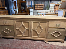 Load image into Gallery viewer, This charming large oak sideboard has been returned to its natural finish and could shine even more with a coat of wax. It offers ample storage with two drawers, one double cupboard, and two single cupboards. Being a used piece, it shows some signs of wear like missing trim and a small bit of wood beneath one drawer, which only enhance its character and appeal.

Overall Dimensions

229cm wide x 52cm deep x 85cm high

DELIVERY AVAILABLE      

For our other items see our website https://fossewayfurniture.co.
