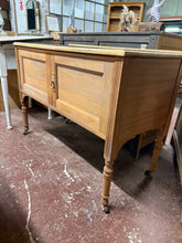 Load image into Gallery viewer, A beautiful stripped mahogany washstand revealing the wood's natural grain and character. Features a practical double cupboard for storage, a removable glass top, and smooth-rolling castors for convenient repositioning. The bare wood finish offers an authentic vintage aesthetic and accepts wax or oil treatments to suit your décor. An elegant addition to period homes or those seeking genuine antique charm.

Delivery Available

Overall Dimensions

105cm wide x 50cm deep x 76cm high

