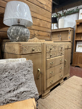 Load image into Gallery viewer, A striking Art Deco sideboard in oak, stripped to reveal its natural grain and warm patina. This substantial piece features seven dovetail-jointed drawers and two single cupboards, offering generous storage for dining rooms, living spaces, or hallways. The bare wood finish showcases authentic craftsmanship and period character—a light wax coat will enhance protection and lustre. Includes original key. A timeless statement piece with genuine vintage appeal.

Delivery Available

Overall Dimensions

153cm wide

