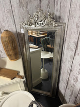 Load image into Gallery viewer, This striking silver-framed mirror features a cherub design that serves as an eye-catching focal point in any room. Built to last, the piece is in good structural condition and ready to display. A timeless statement piece that combines decorative appeal with practical functionality.

Delivery Available

Overall Dimensions

53cm wide x 142cm high

