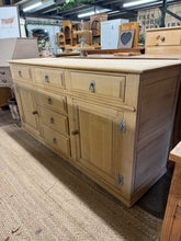 Load image into Gallery viewer, Crafted from solid oak and restored to its authentic natural finish, this exceptional sideboard combines timeless elegance with practical functionality. The robust construction features six dovetail-jointed drawers and two spacious cupboards, each fitted with an internal shelf, delivering generous storage solutions for any room. Its substantial weight reflects the quality craftsmanship and durability. A protective wax finish will enhance both its appearance and longevity.

Overall Dimensions

168cm wide x 5

