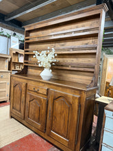 Load image into Gallery viewer, Solid oak dresser in structurally sound condition. Features 3 shelves in the top section, one dovetail-jointed drawer, and 3 cupboards below. Includes original key. The piece shows honest wear with minor marks and some damage to one leg—nothing affecting functionality. Internal shelves would benefit from light restoration. Top section separates from base for convenient moving and transport.

Delivery Available

Overall Dimensions

183cm wide x 47cm deep x 215cm high

