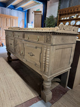 Load image into Gallery viewer, This exceptional large solid oak sideboard makes a striking statement piece for any room. Stripped back to its natural state, the wood grain is fully exposed and ready for your personal finishing touch—a coat of wax will enhance protection and patina. Generously proportioned with two long drawers, one short drawer, and three cupboards, it offers substantial storage for dining rooms, living spaces, or hallways. Built to last, this substantial piece combines timeless craftsmanship with practical functionality
