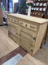 Load image into Gallery viewer, This oak sideboard has been stripped to bare wood, revealing its bare natural self. Two dovetail-jointed drawers sit above a double cupboard with a single shelf inside, providing ample storage space. The piece is in good structural condition and ready for use, though a protective wax finish is recommended to preserve the wood. A practical, characterful piece suitable for various interior styles.

Delivery Available

Overall Dimensions

122cm wide x 43cm deep x 89cm high

