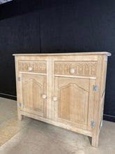 Load image into Gallery viewer, A beautiful stripped oak sideboard with authentic character. This piece has been carefully restored to reveal the natural wood grain, with minor patina marks that add to its charm. Features two dovetail-jointed drawers positioned above a spacious double cupboard, offering generous storage for dining rooms or living spaces. The natural finish may benefit from a protective coat of wax to enhance durability and lustre. A versatile addition to traditional or contemporary interiors.

Delivery Available

Overall 
