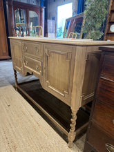 Load image into Gallery viewer, Discover the timeless appeal of this stripped oak sideboard, ready for your personal finishing touch. Featuring authentic barley twist legs and a spacious interior with two cupboards and two drawers, it offers practical storage with character. The natural wood finish showcases the grain beautifully, though a protective wax coat is recommended. Structurally sound with minor marks that add to its vintage charm, this piece comes complete with its original key. Perfect for those seeking genuine period furniture
