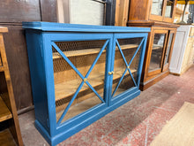 Load image into Gallery viewer, A charming pine bookcase with authentic country character. Finished in blue paint with some wear that adds to its rustic appeal, this piece is structurally solid and ready for use. Two generous internal shelves provide practical storage for books, decorative items, or collectables. Perfect for those who appreciate vintage furniture with genuine patina and character.

Delivery Available

Overall Dimensions

123cm wide x 29cm deep x 83.5cm high&nbsp;&nbsp;

