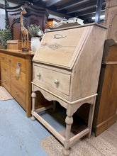 Load image into Gallery viewer, A charming narrow oak bureau with authentic character. This piece has been stripped back to reveal beautiful natural wood grain and patina. Features a pull-down writing desk above a single dovetail-jointed drawer, offering practical storage and workspace. Structurally sound and in excellent condition. The bare wood finish invites personalisation — consider applying wax or oil to enhance protection and lustre. A versatile addition to period homes or contemporary spaces seeking vintage appeal.

Delivery Avail
