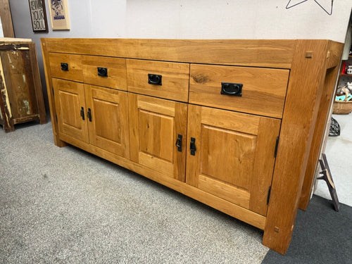 This spacious and sturdy oak sideboard is a charming addition to any home, offering both style and practicality. Despite being pre-owned, it remains in good overall condition with only minor marks that add character without detracting from its appeal. The design includes four roomy drawers positioned above two cupboards, each equipped with a shelf to help organize your belongings efficiently. Its solid construction ensures durability, making it perfect for storing dining essentials, linens, or other househo