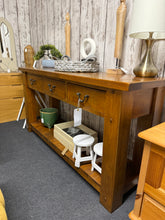 Load image into Gallery viewer, This substantial oak hall table combines practicality with timeless appeal. Featuring three spacious drawers and a lower shelf, it offers generous storage for entryway essentials. Crafted from oak, the piece is structurally sound and ready to serve. As a pre-loved item, it bears the honest character of age with minor surface marks—a testament to its durability and authentic charm. An understated addition to any hallway or living space.

Delivery Available

Overall Dimensions

153cm wide x 46cm deep x 77cm h
